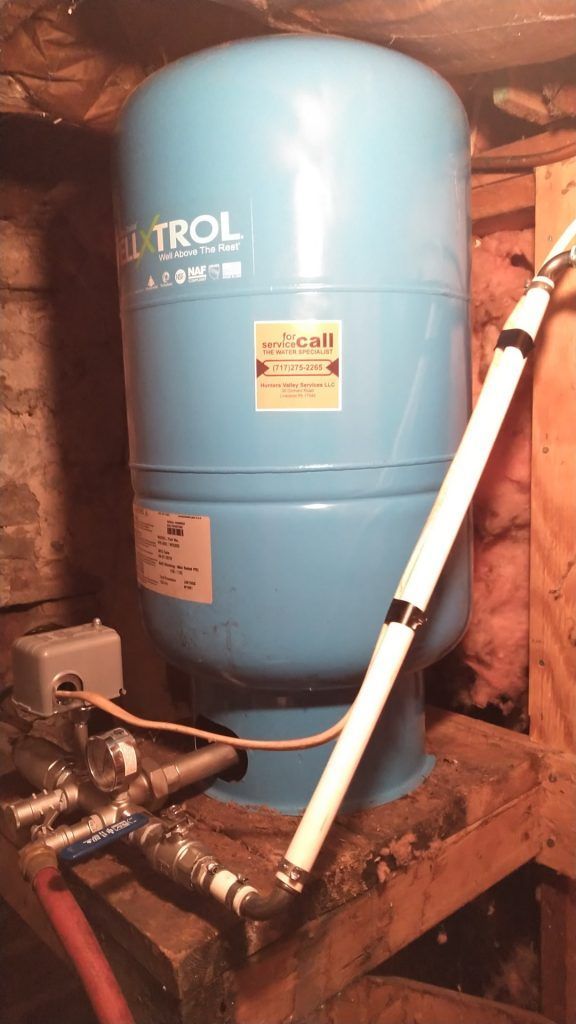 Blue water pressure tank, pipes, and control box in a basement setting.