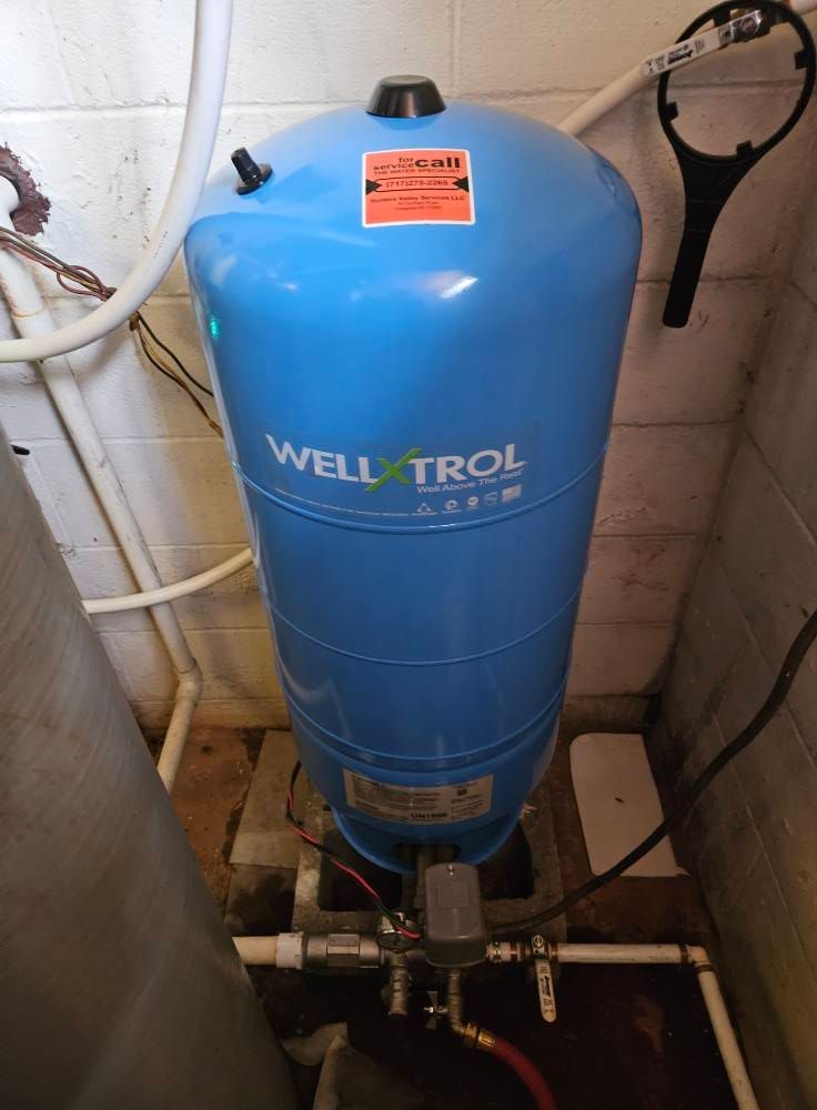 Blue Well-X-Trol water pressure tank with white pipes on a concrete floor in a basement.