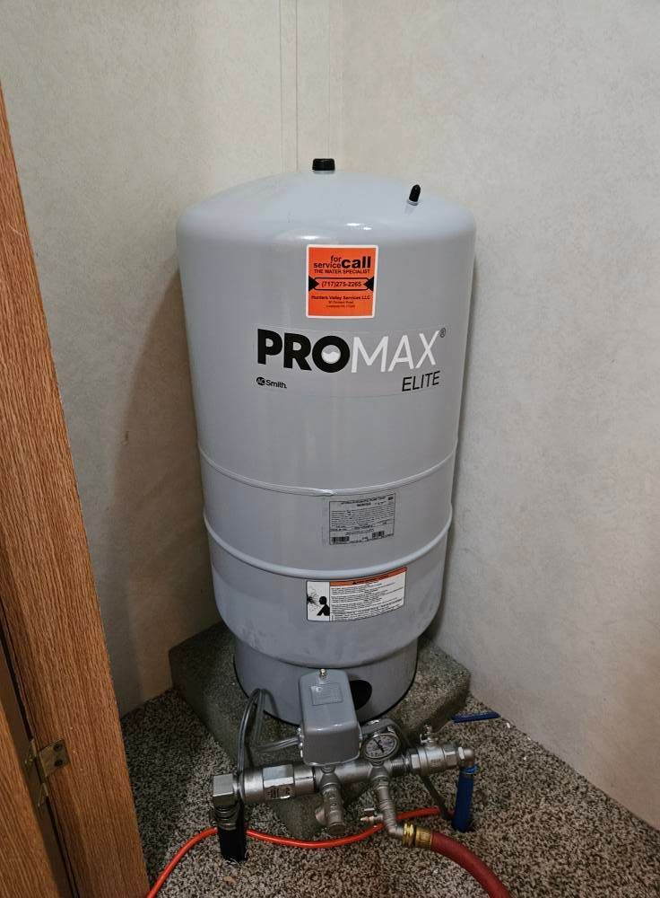 A water pressure tank  in a corner, with pipes and gauges below.