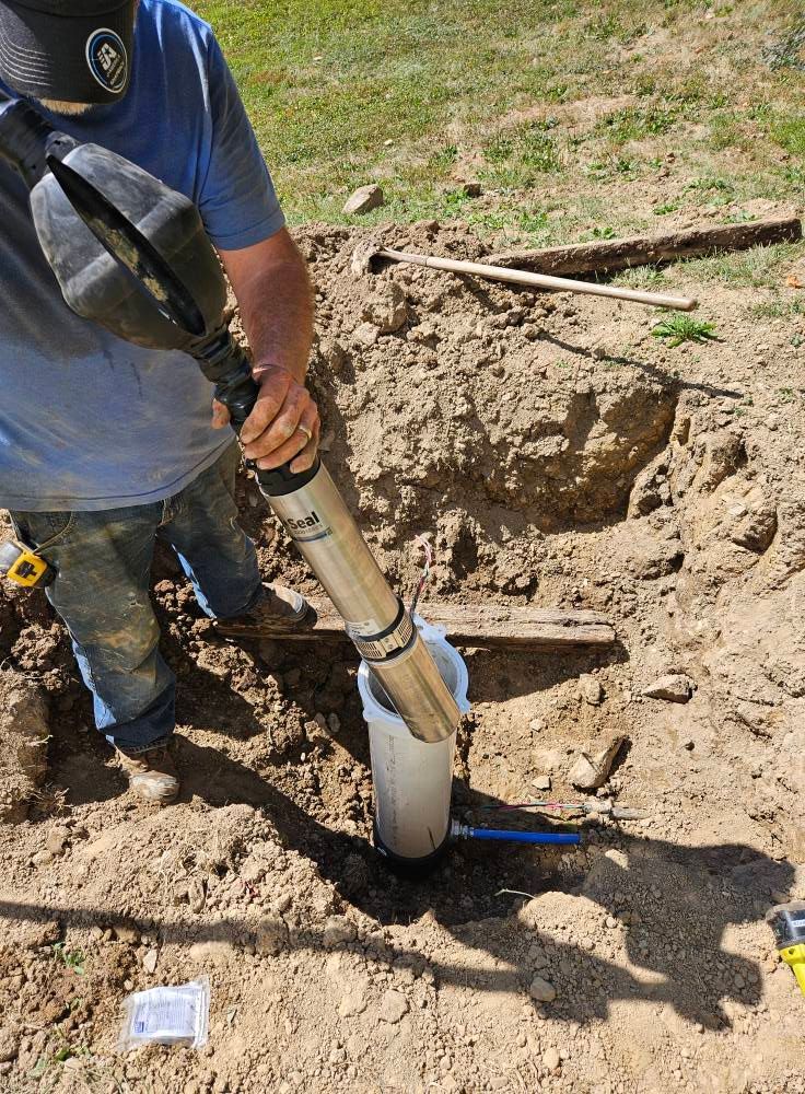 Person using a soil sampler in a hole outdoors.