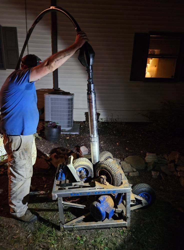 Man operating well pump at night, holding black hose. Pump is on a wheeled cart.