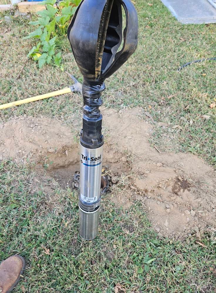 A Tex-Steel well pump is being installed in a hole in a grassy yard.
