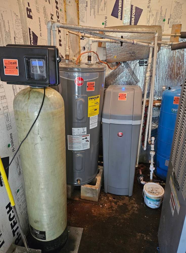 Plumbing equipment: water heater, water softener, and filter in a utility room with exposed insulation.