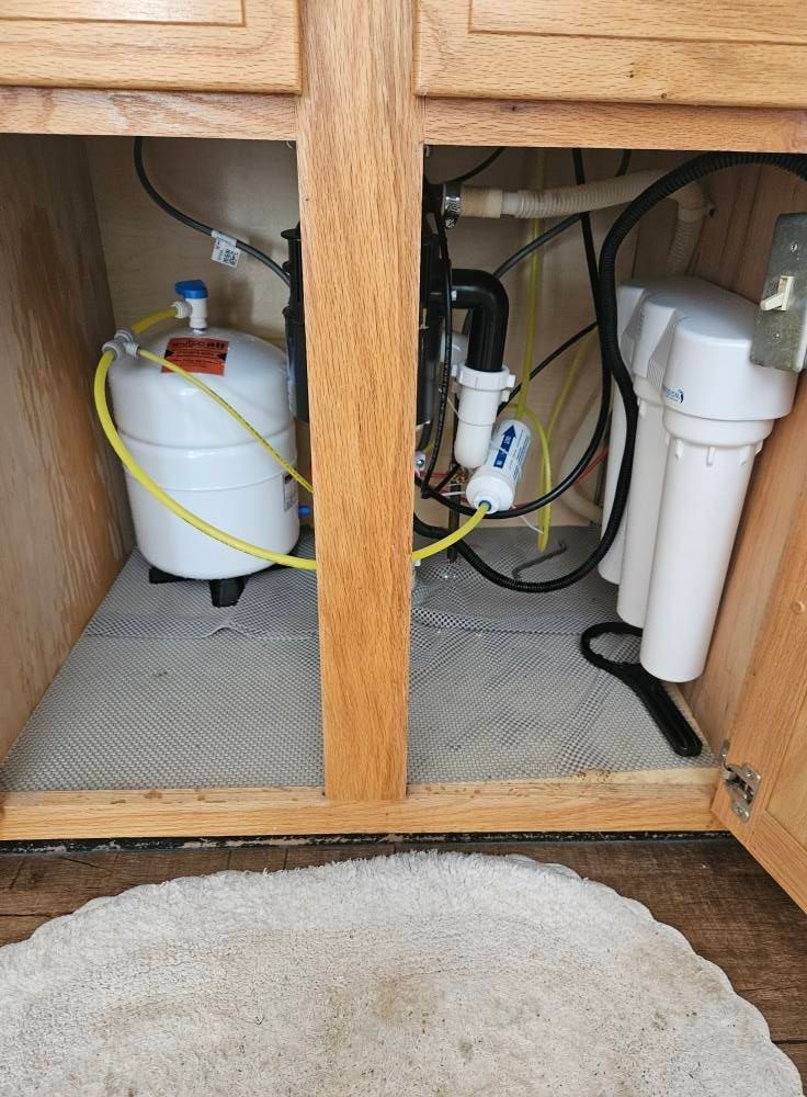 Undersink cabinet with water filter, storage tank, and plumbing.  Yellow and white components.