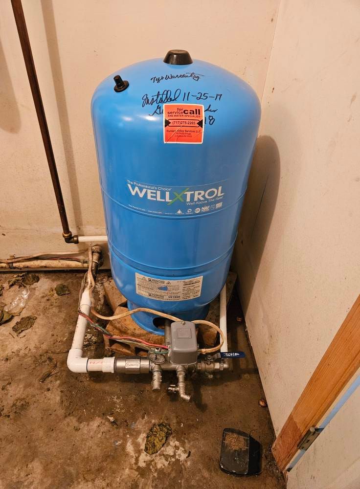 Blue Well-X-Trol water pressure tank in a basement corner, pipes visible.