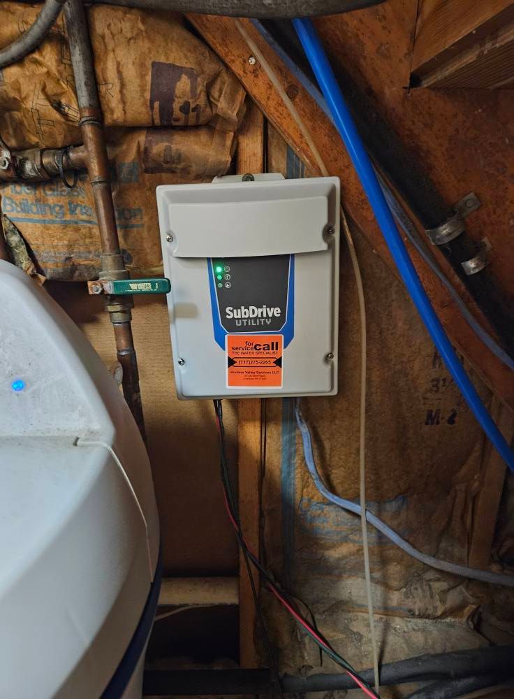 A SubDrive Connect well pump control box mounted on a wooden wall. Wires and pipes surround it.