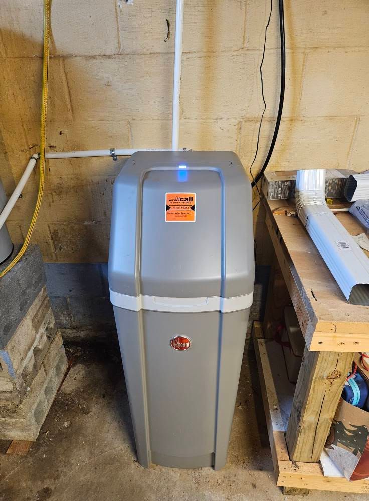 A gray water softener unit in a basement setting, with visible plumbing.