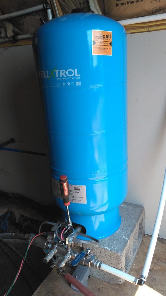 Blue water pressure tank with attached plumbing and a screwdriver, indoors.