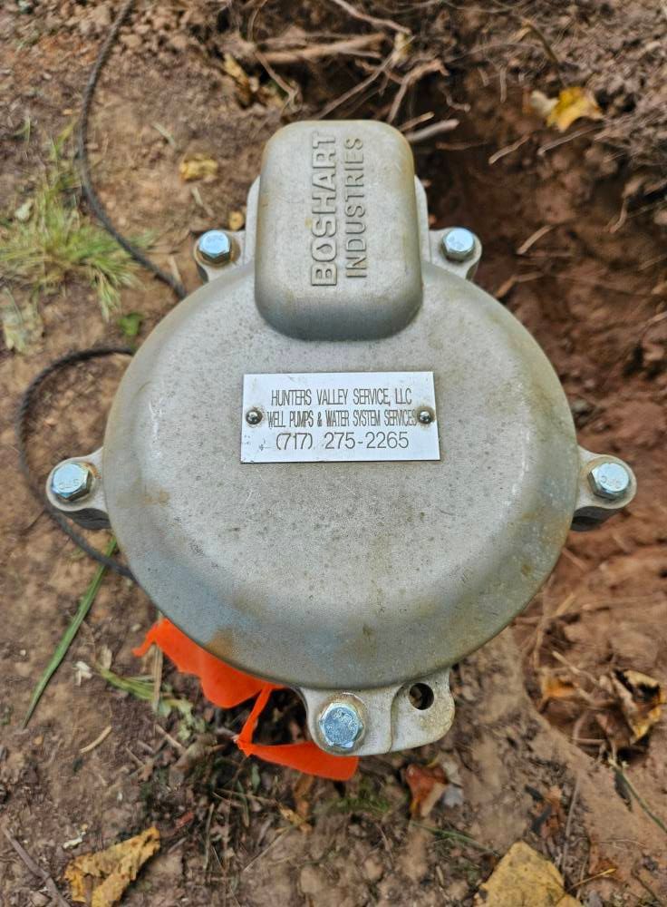 Silver box in a hole in the ground, orange flags visible.