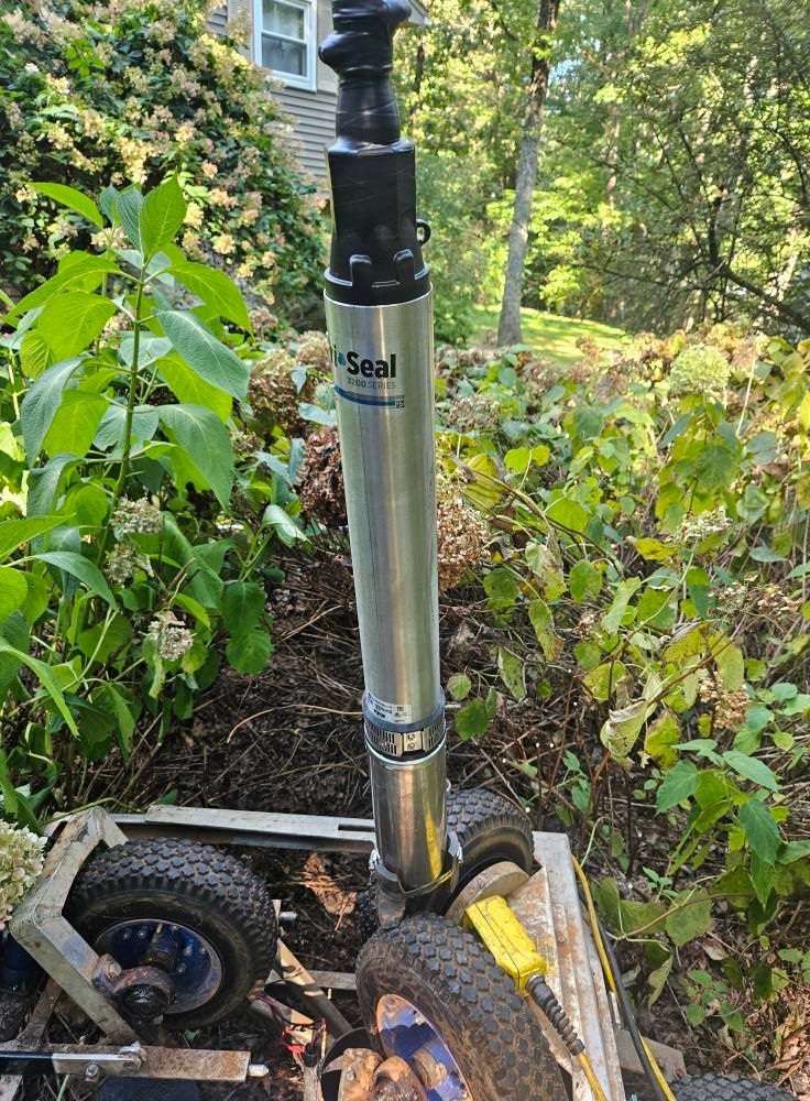 A silver Seal pump attached to a cart with blue wheels, in a garden setting.
