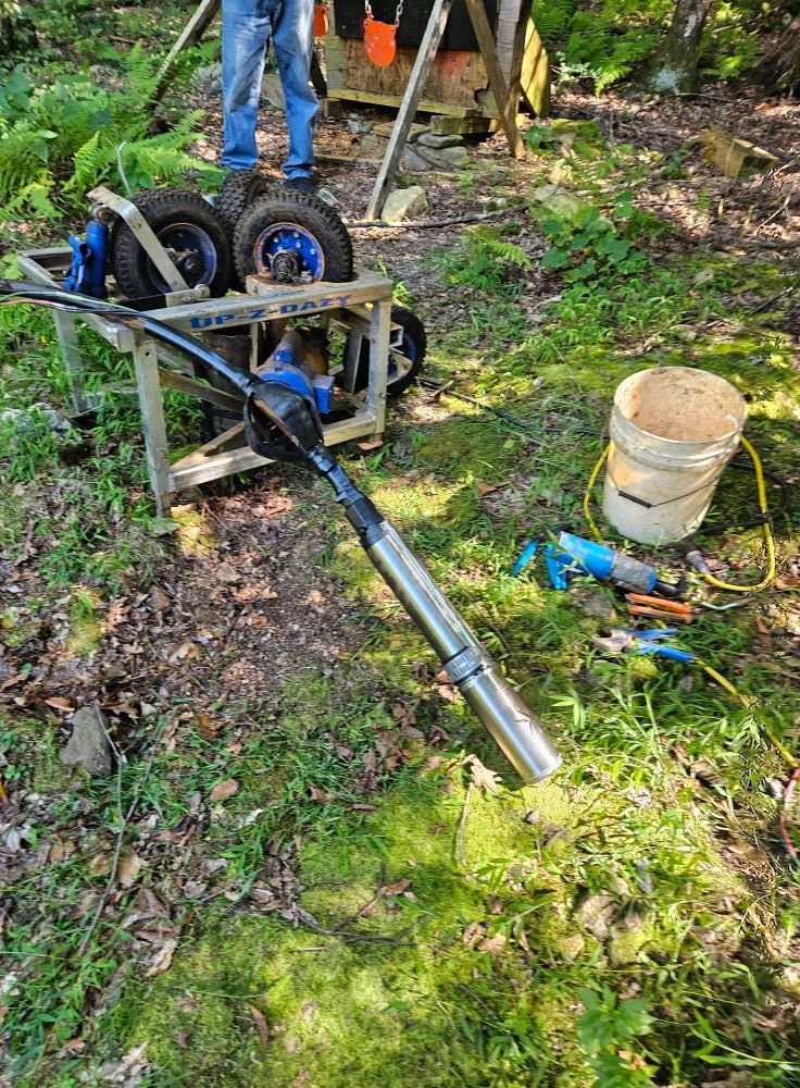Well pump and tools on ground near person and wooded area.