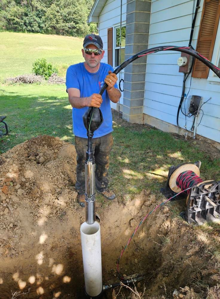 Man lowering well pump into a dug hole next to a house.