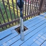 A boat motor is installed through a square hole cut in a blue wooden deck, outdoors near a railing.