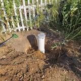 White pipe protruding from the ground near a white picket fence in a garden.