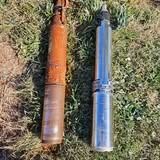 Two artillery shells, one rusted, the other shiny, lying on grass.
