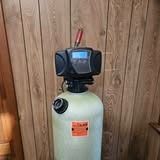 Water softener tank with digital display against wood paneling.