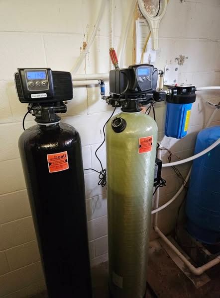 Two water filtration tanks with digital displays, plumbing, and a blue filter in a utility room.
