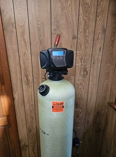 Water softener system against wood paneling. Cylindrical tank with digital control panel.