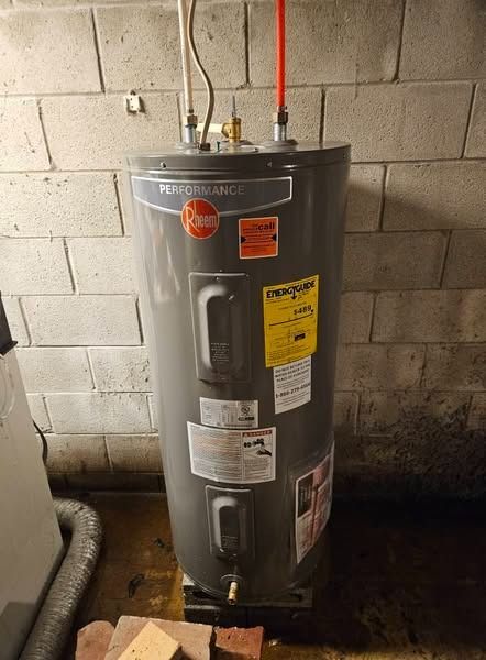 A Rheem water heater, gray and cylindrical, stands against a cinder block wall in a basement.