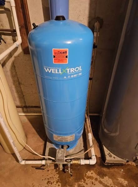 Blue Well-X-Trol water pressure tank in a basement, surrounded by pipes and a white foundation.