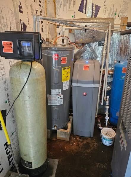 Water softening system in a basement.  Includes softener, water heater, filter, and other plumbing against a wall.