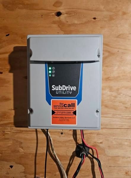 A gray SubDrive Utility box mounted on wood paneling, with wires connected and indicator lights lit.
