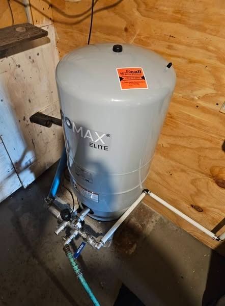 Gray ProMax Elite water pressure tank with white pipes in a basement.