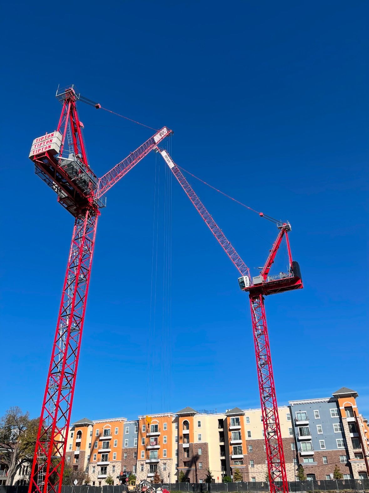 Two red cranes are sitting in front of a building under construction.