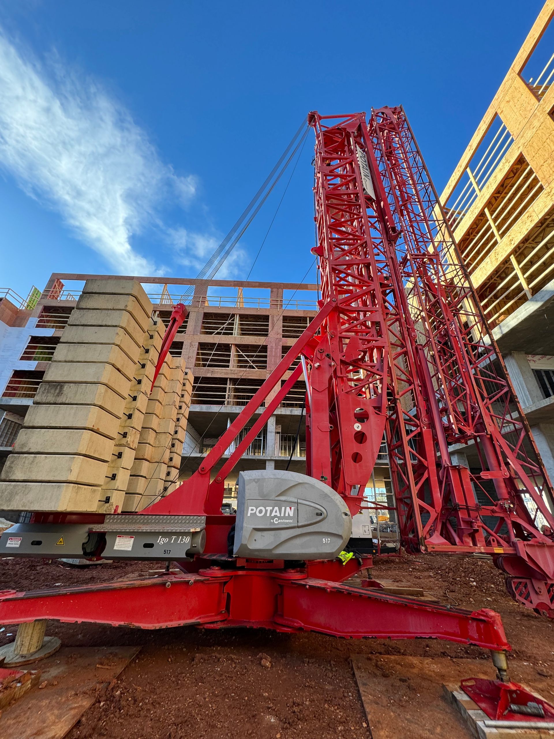 A large red crane is sitting in front of a building under construction.