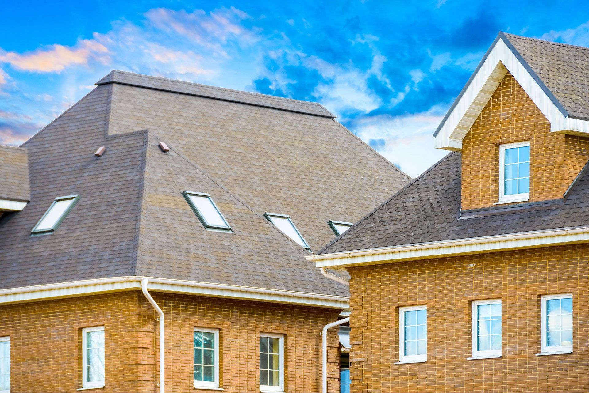 Brick buildings with brown shingled roofs and blue sky. Several windows and skylights are visible.
