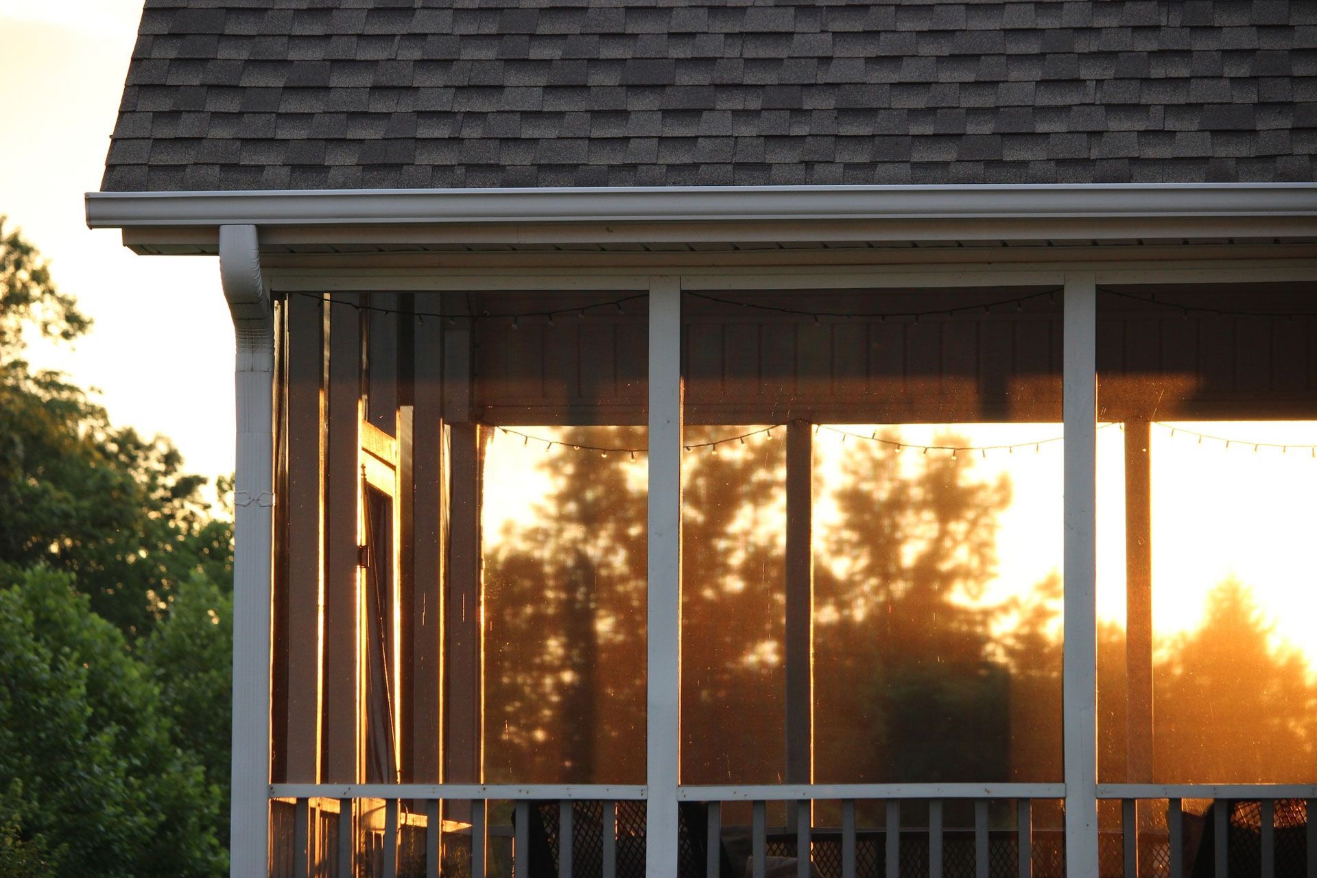 Screened porch with reflections of a sunset. Sunlight casts golden hues across the screens and onto the wooden structure.