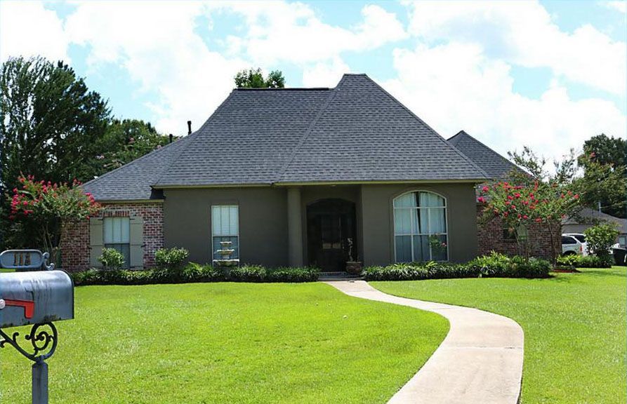 A light-brown, one-story house with a new roof, red brick accents, and a curving sidewalk.