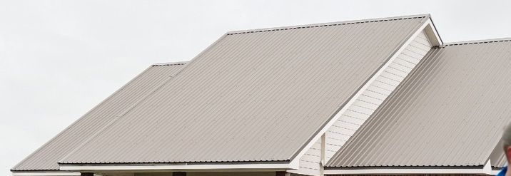 Two roofers in blue shirts are working on a roof with a metal and shingle section. They are holding boxes and buckets.