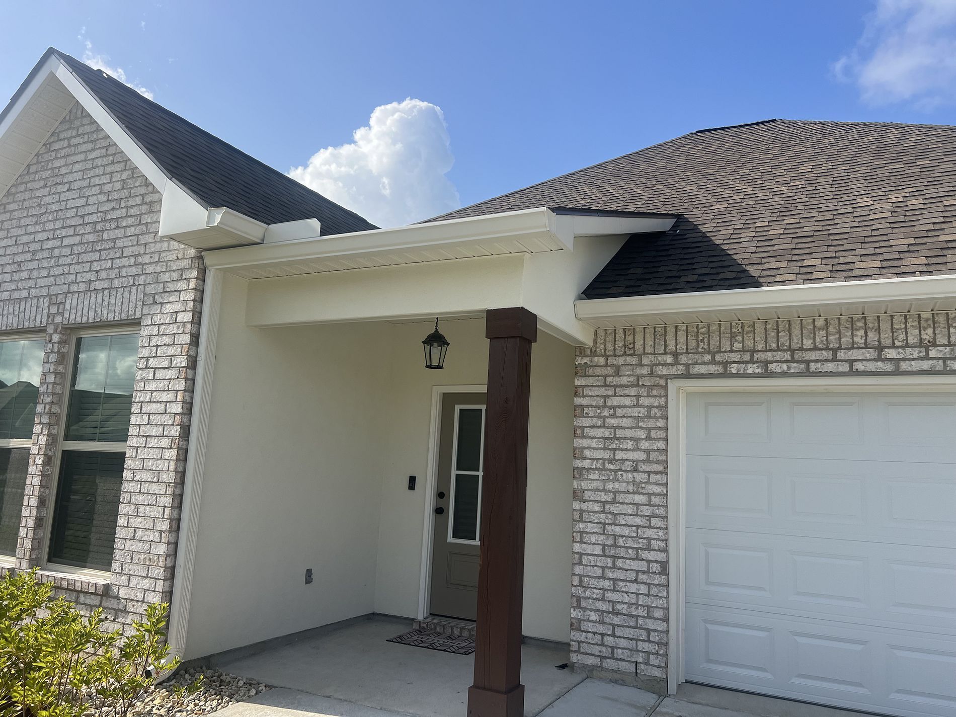 A house with white brick, a white garage door, and a brown front door under a covered porch with a brown post.