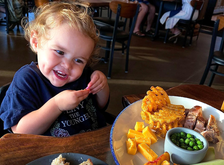 A little boy sitting at a table with a plate of food