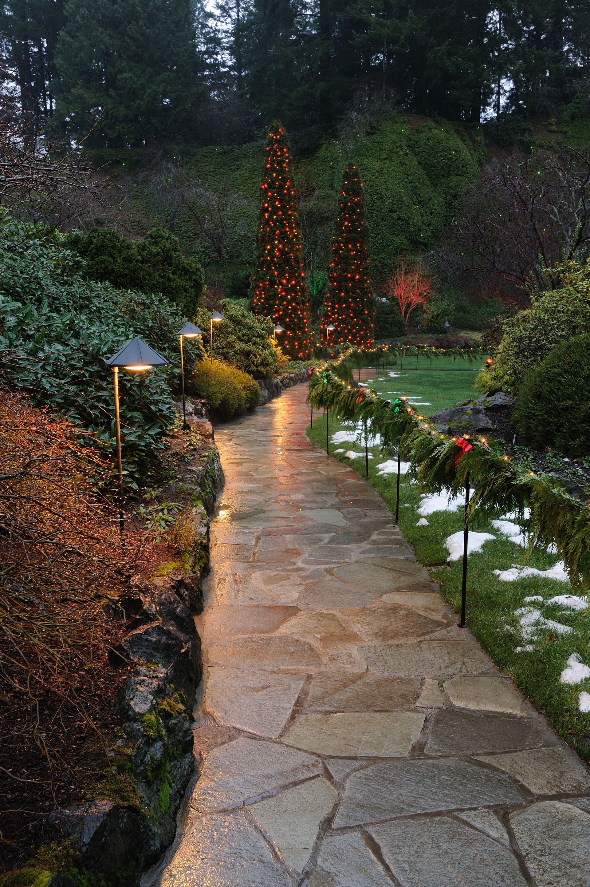 Stone garden path lit by orange lights, winding through lush greenery at dusk.