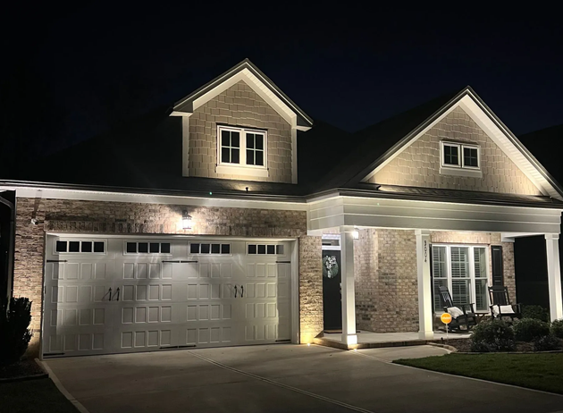 Well-lit suburban house at night with stone facade, garage, and front porch lights