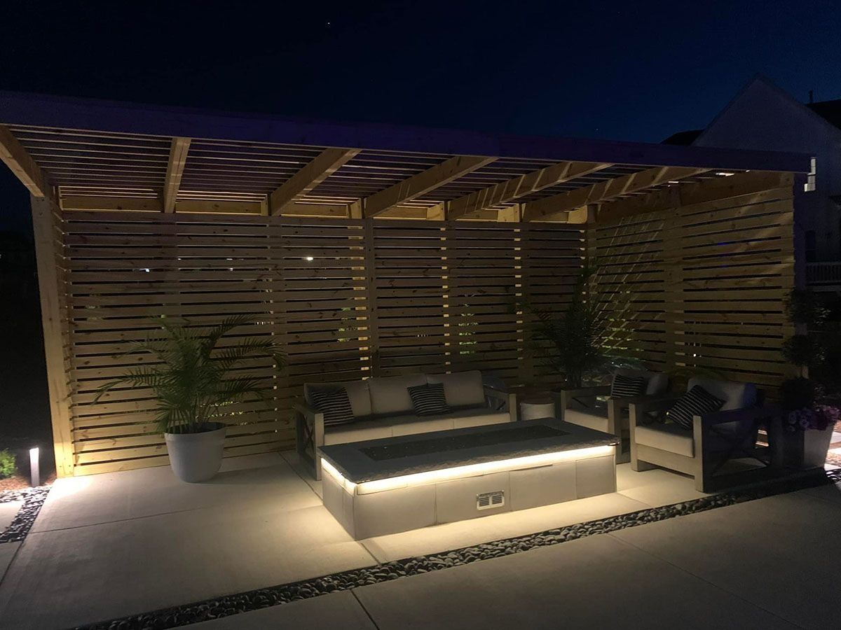 Nighttime outdoor lounge with wooden slat pergola, lit seating, and potted plants.