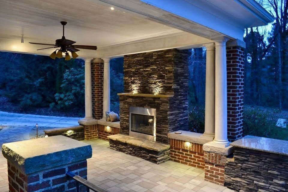 Covered patio with stone fireplace, white columns, ceiling fan, and blue evening lighting
