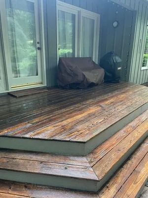 Weathered wooden deck steps leading to a covered porch with sliding glass doors and a grill under a cover
