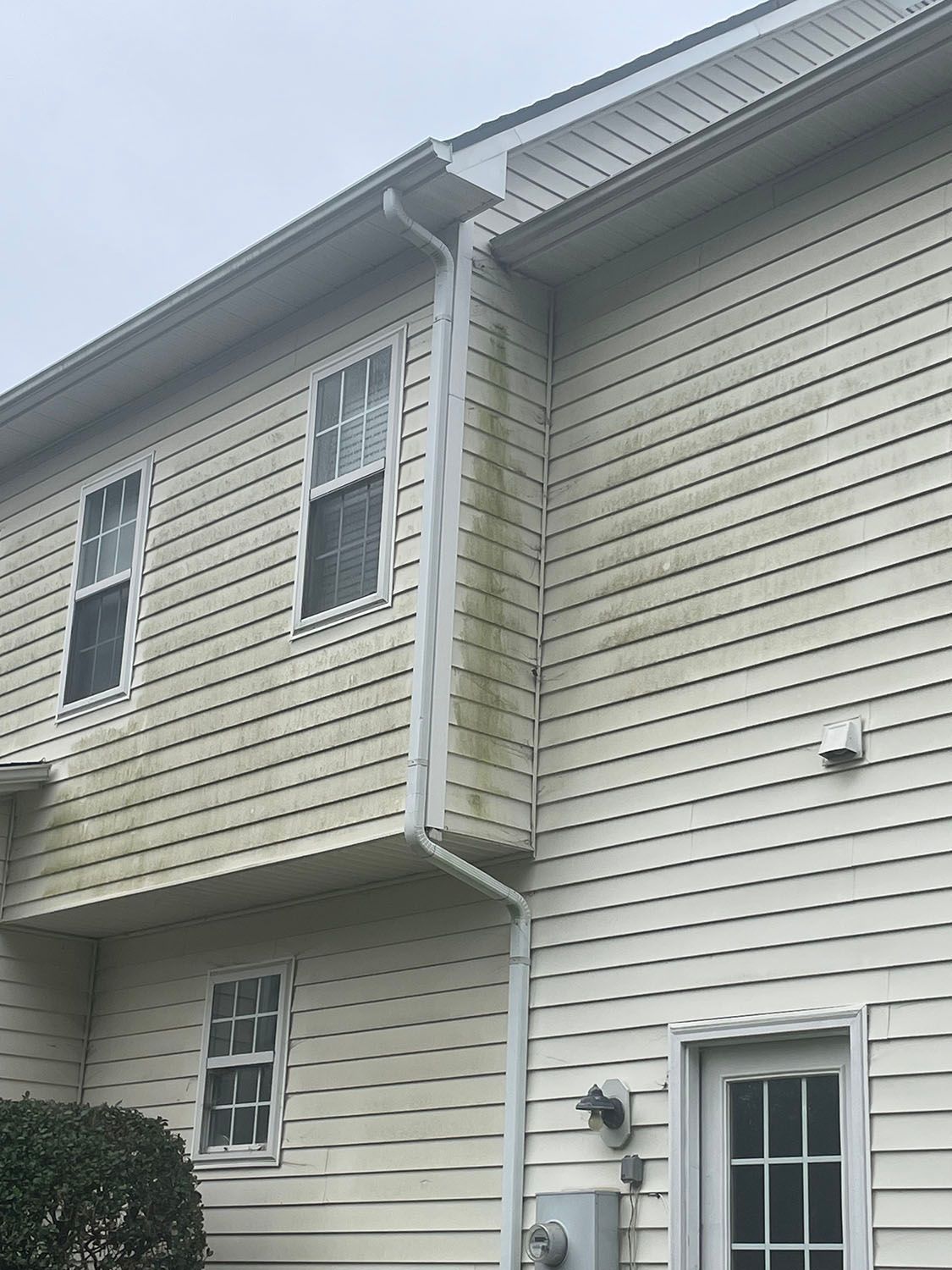 Close-up of a beige house exterior with white siding, windows, and roof eaves.