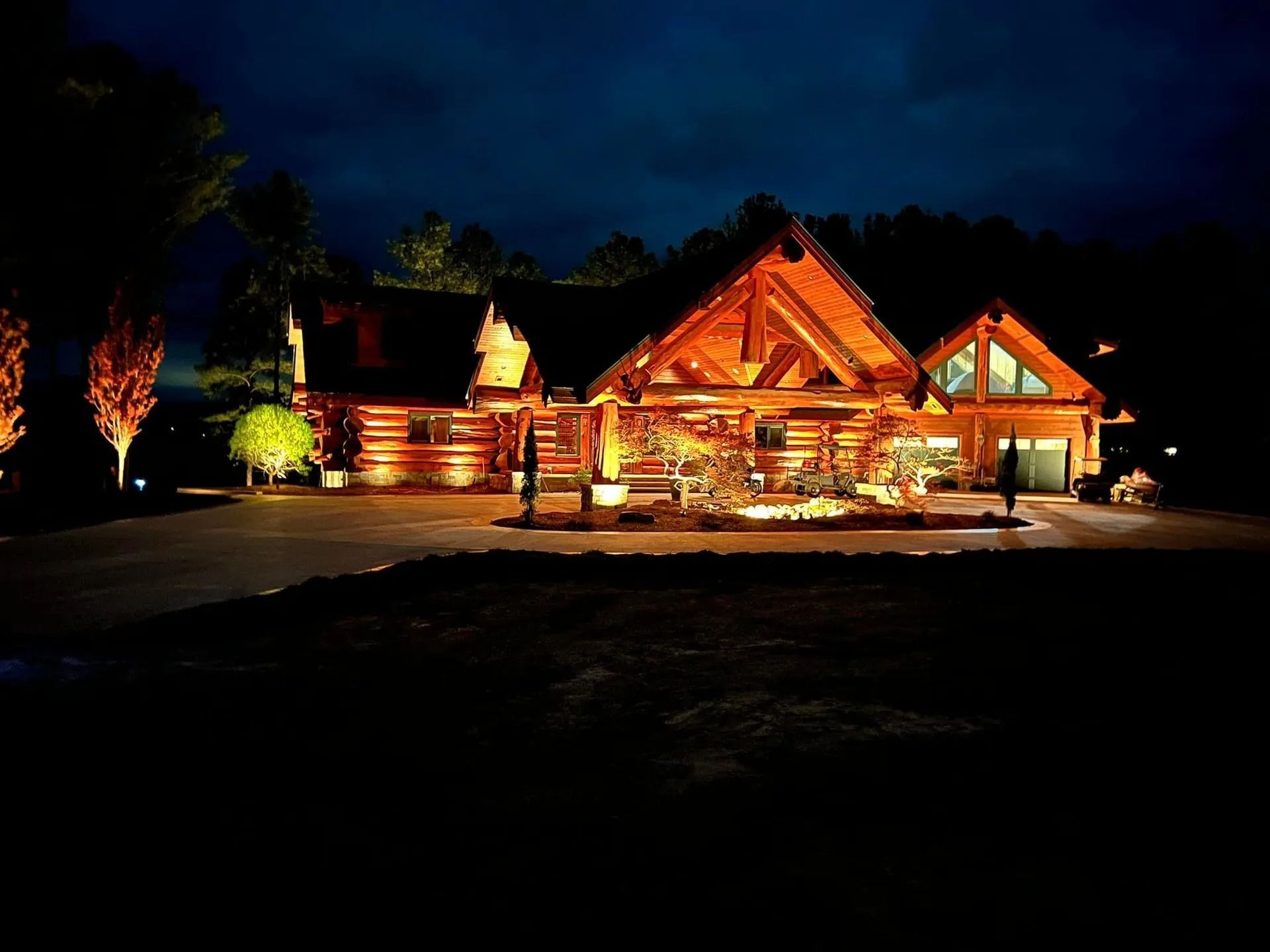 Lit rustic log cabin at night with warm porch lights and trees silhouetted against a dark sky