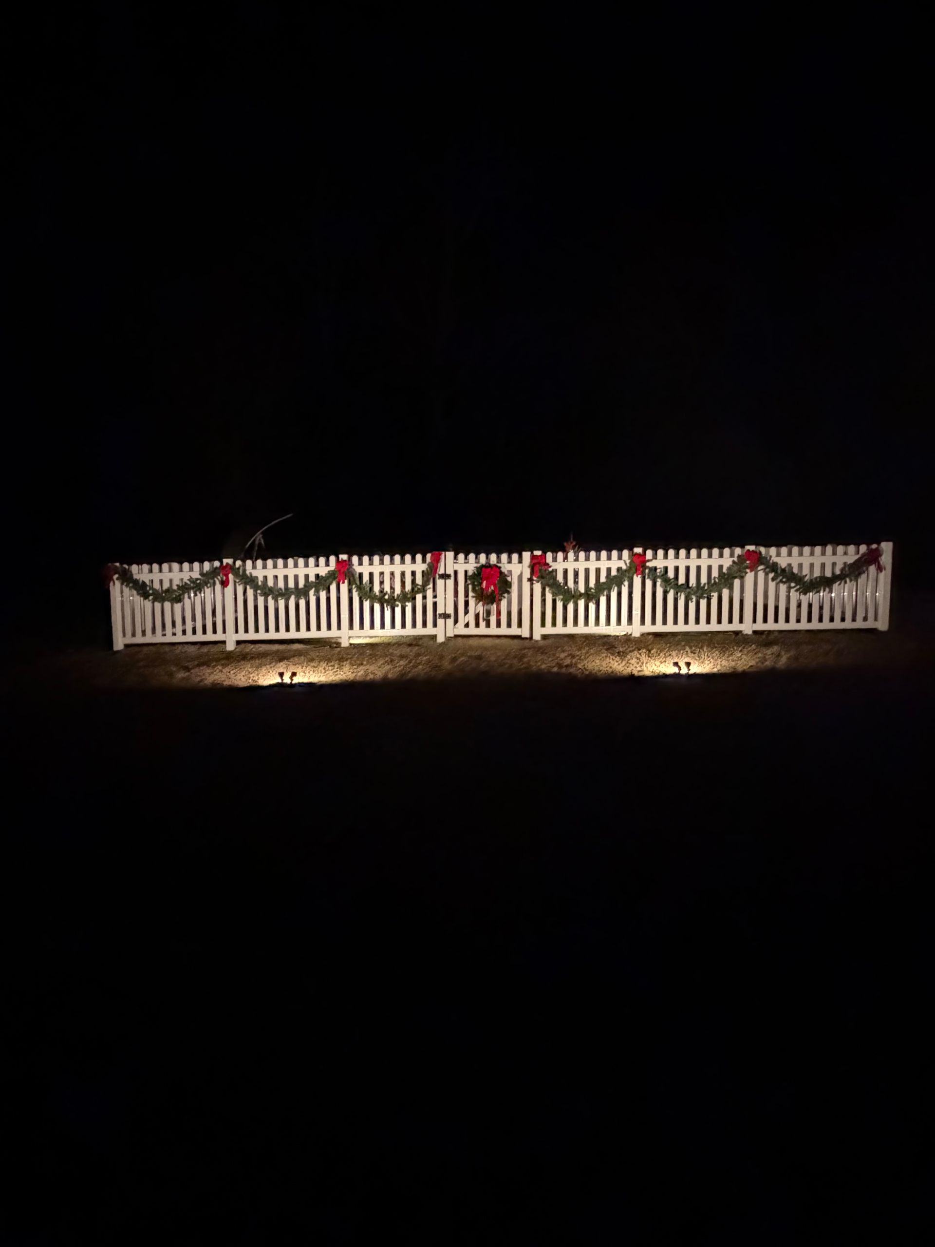 Illuminated white fence with red and green holiday garland against a dark background