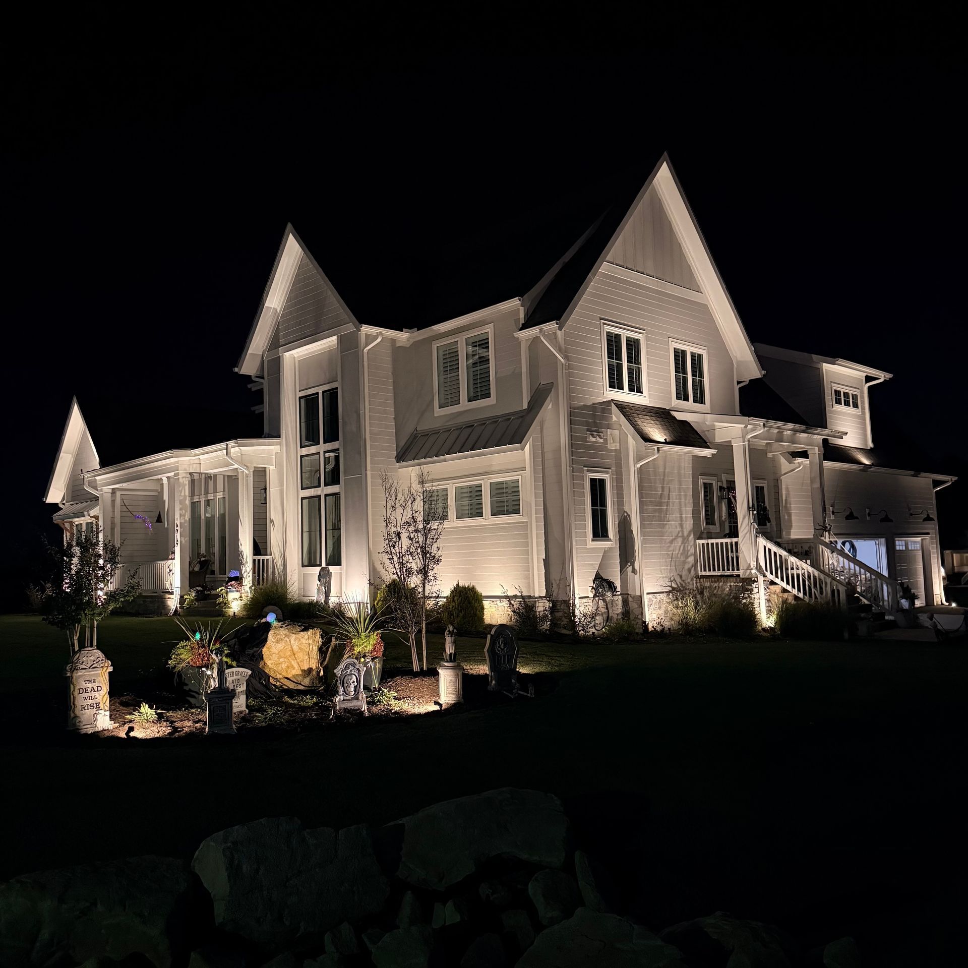 Large white house illuminated at night with front landscaping and dark sky