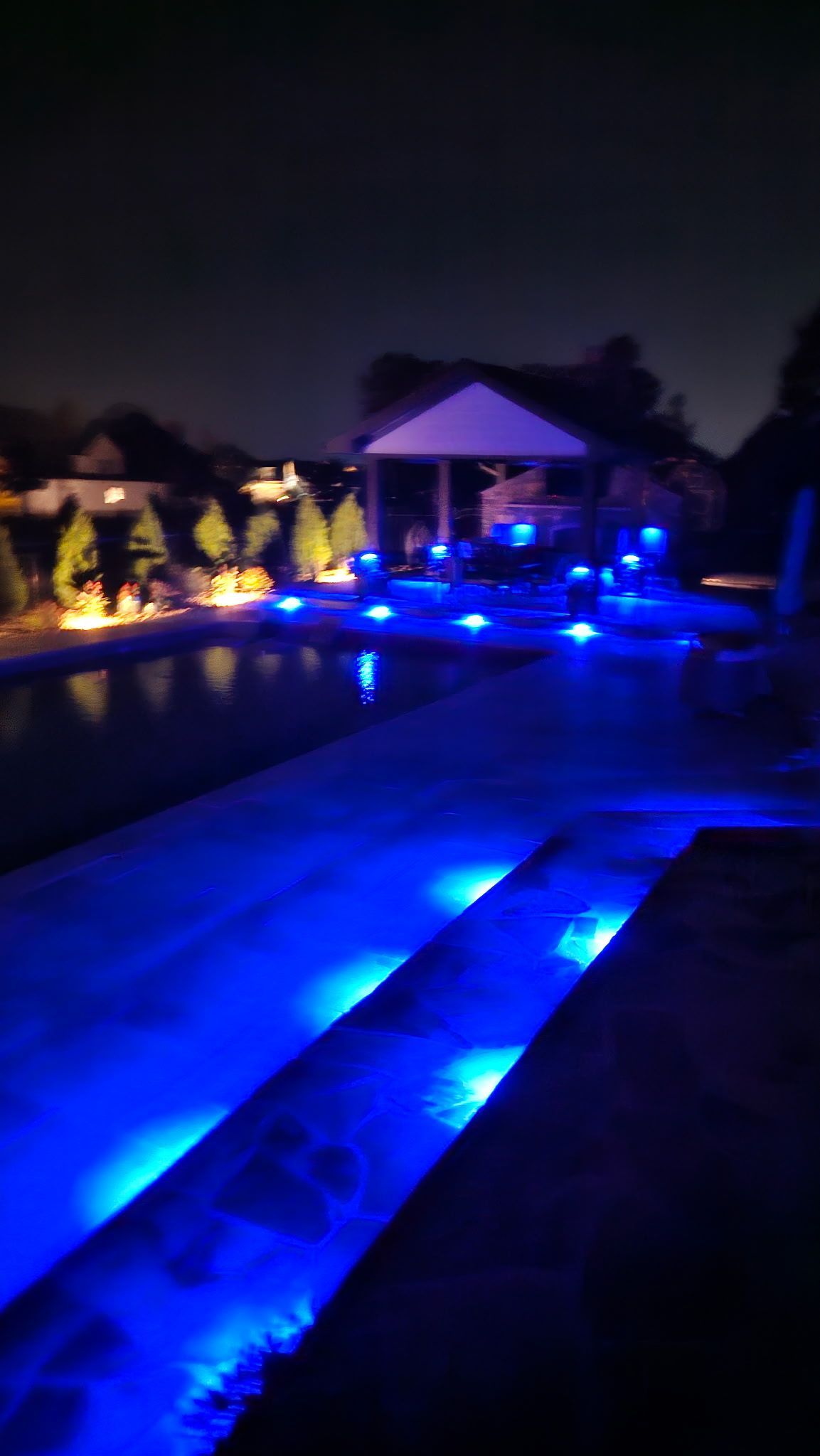 Nighttime resort pool lit with bright blue underwater lights, leading to a pavilion and palm trees.
