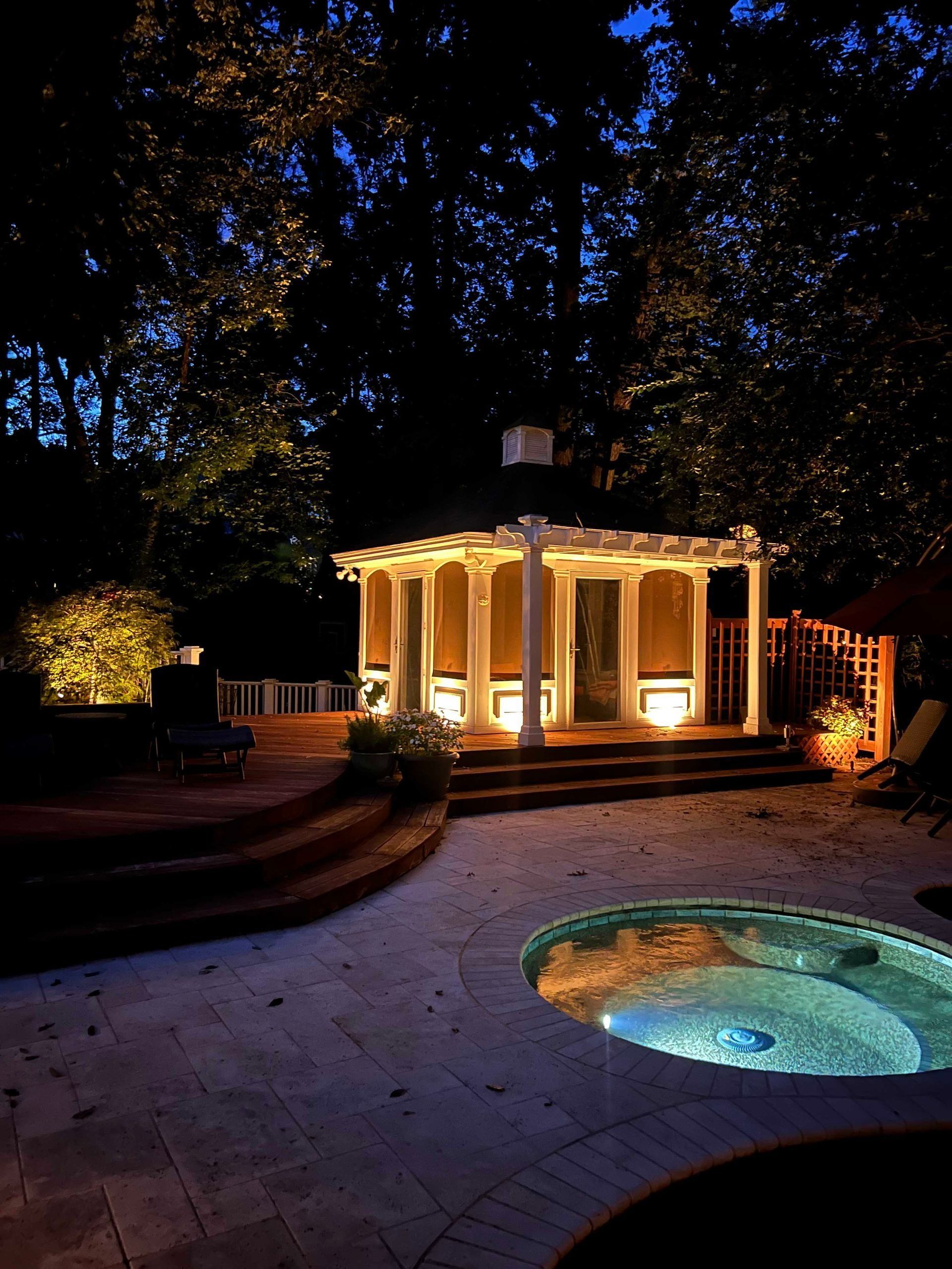 Nighttime patio with a lit gazebo and glowing pool under dark trees
