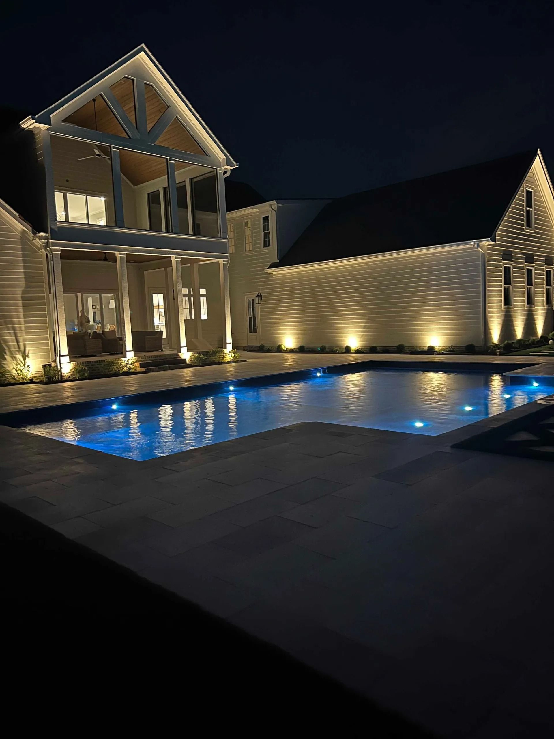 Nighttime view of a lit luxury villa with a glowing pool and reflections on the water