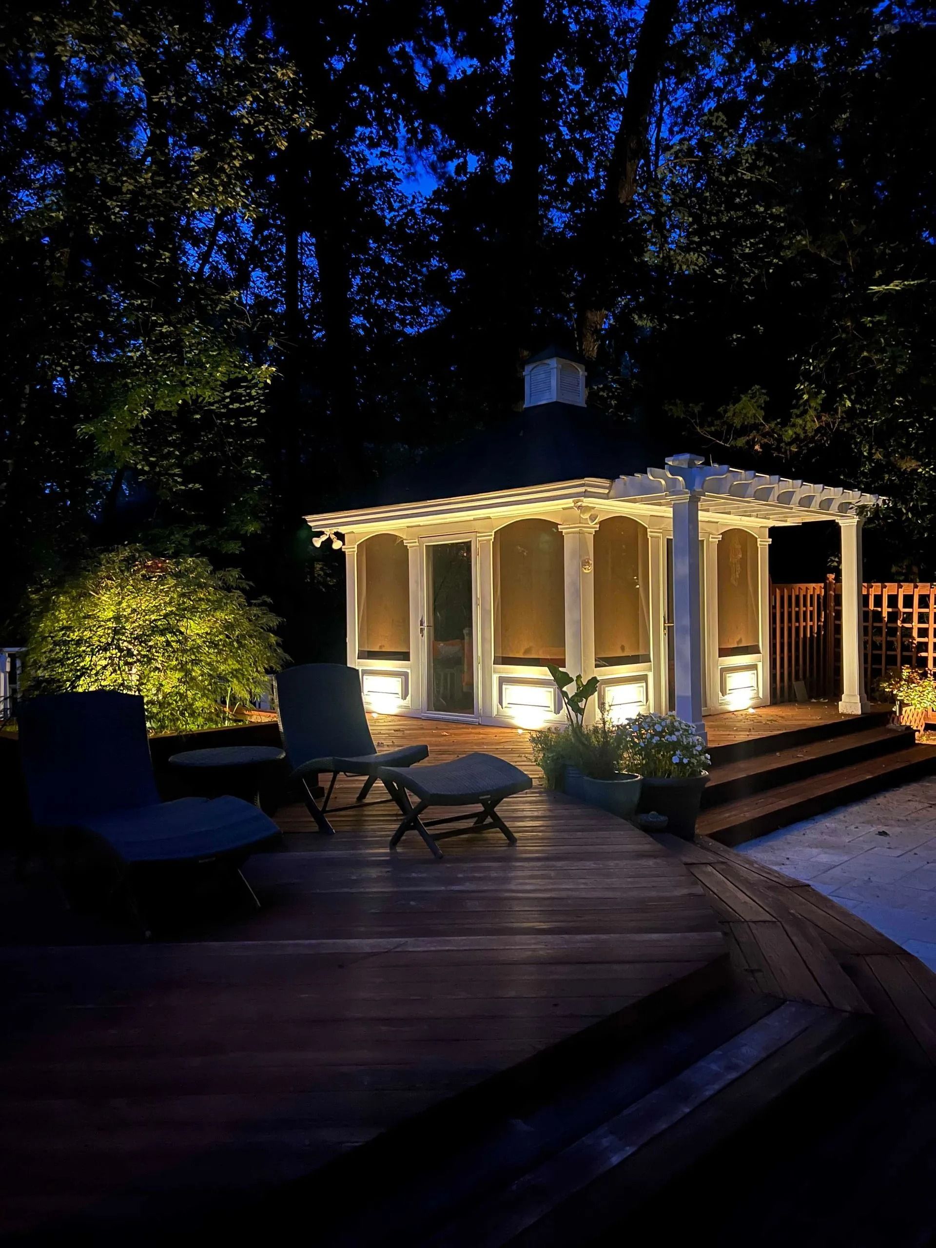 Lit gazebo on a dark wooden deck surrounded by trees at night
