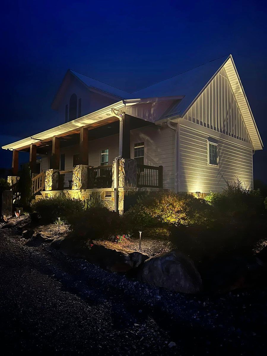 Lit house at night with warm porch lights, stone exterior, and dark blue sky.