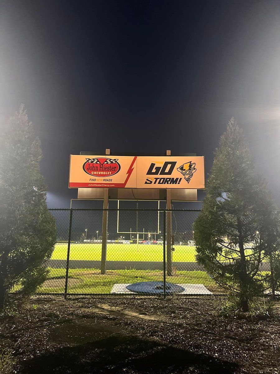 Nighttime sports field scoreboard with bright lights and trees in the background.